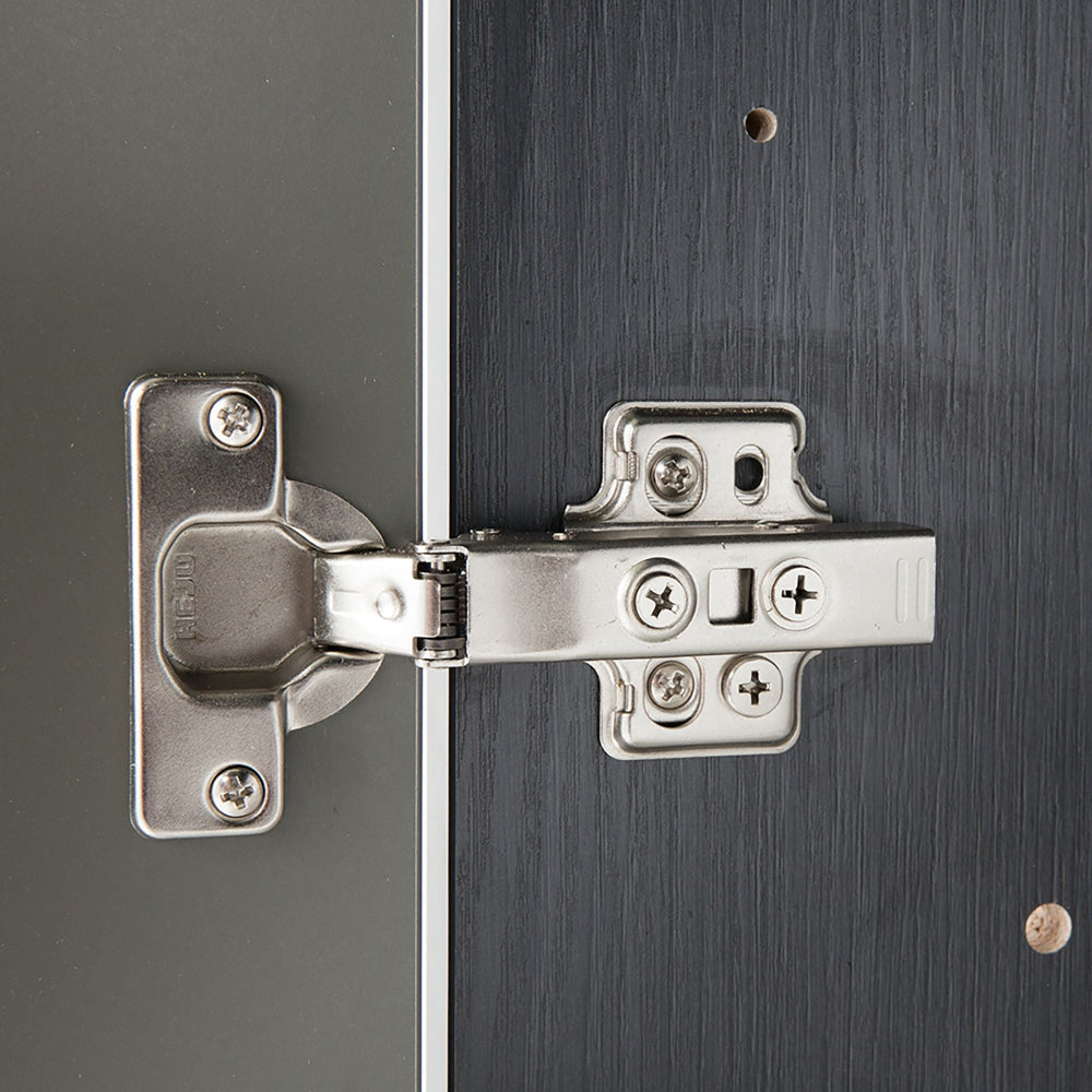 Close-up of a metallic cabinet hinge on a dark wooden surface