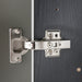 Close-up of a metallic cabinet hinge on a dark wooden surface